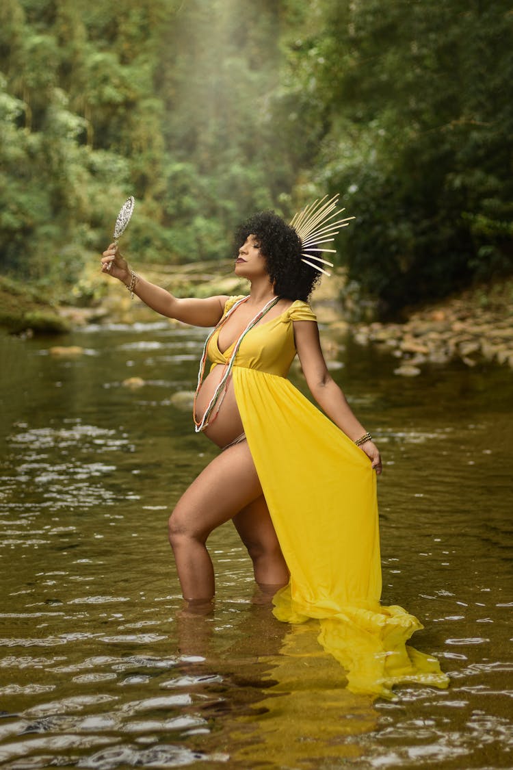 Pregnant Woman Posing While Standing Ankles Deep In Water And Holding A Mirror 