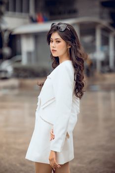 Elegant woman in a white dress posing outdoors with sunglasses.