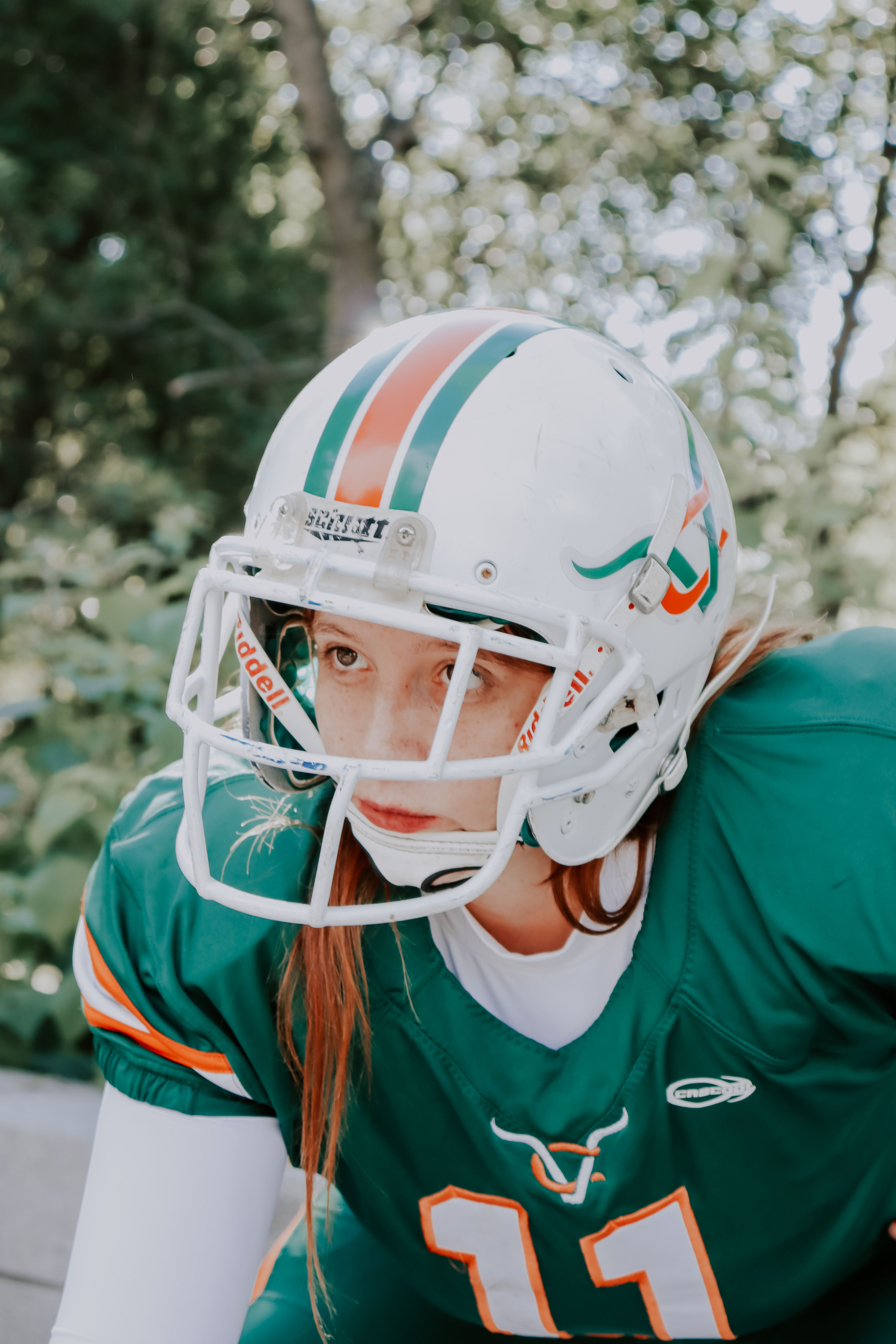 Focused female American football player in green uniform posing outdoors on a sunny day.