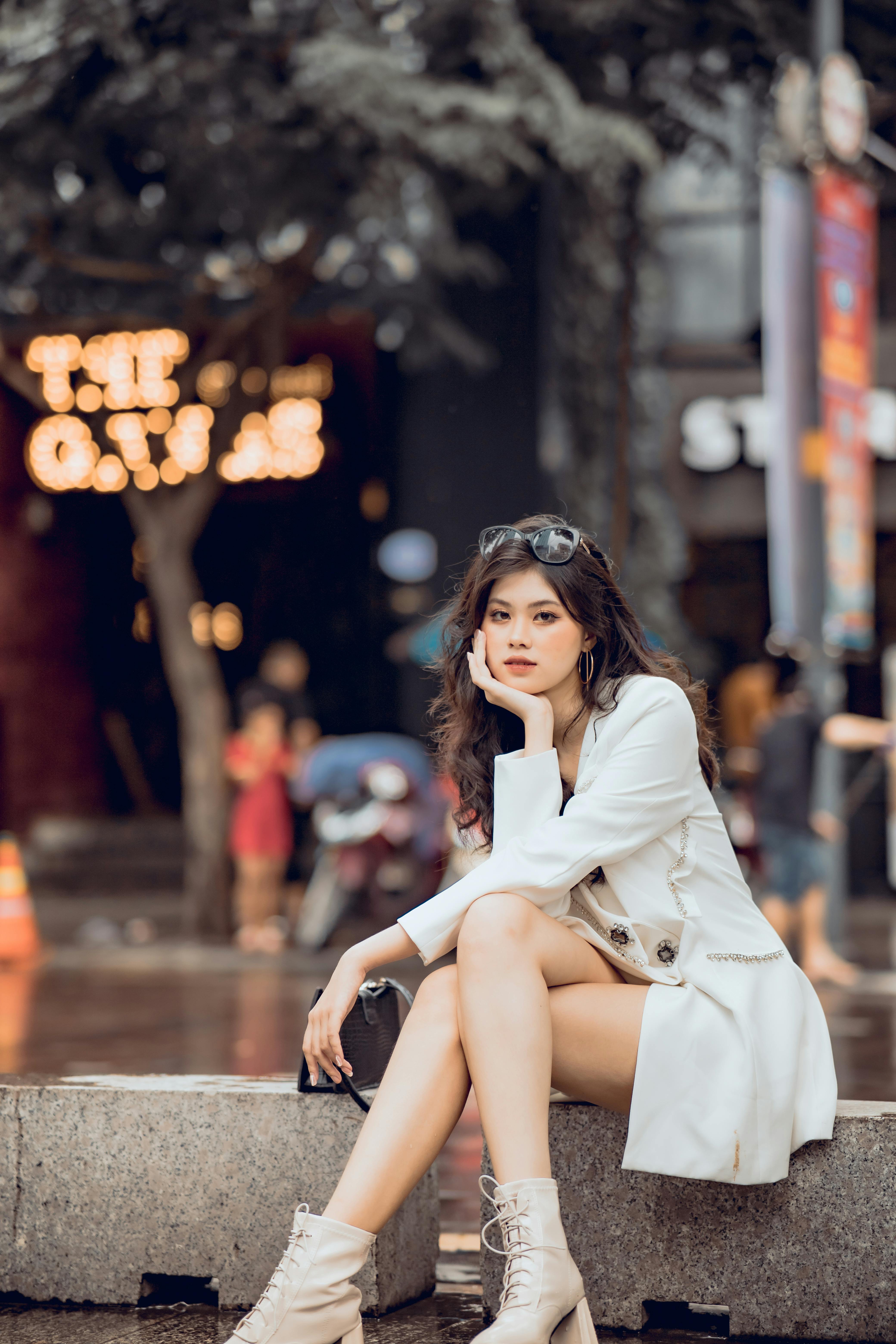 Fashionable young woman in white coat sitting elegantly in an urban setting.