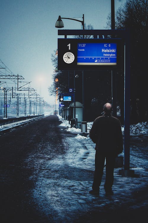 Man Looking at the Information Board at a Bus Stop next to the Railway Tracks