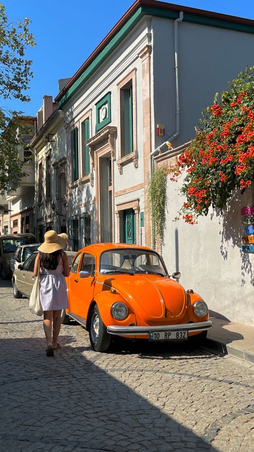 Free A vibrant street scene featuring a vintage orange Volkswagen Beetle parked in Ayvalık, Türkiye. Stock Photo