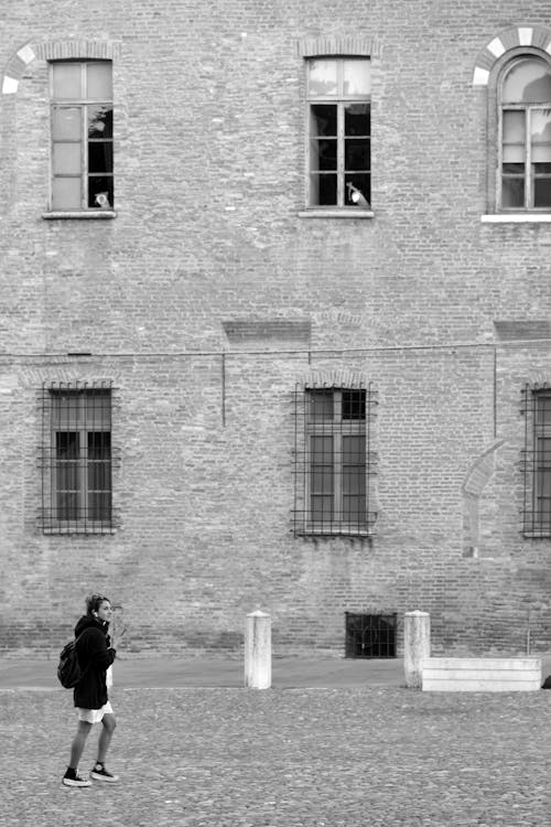 Grayscale Photo of a Person Walking Outside a Brick Building