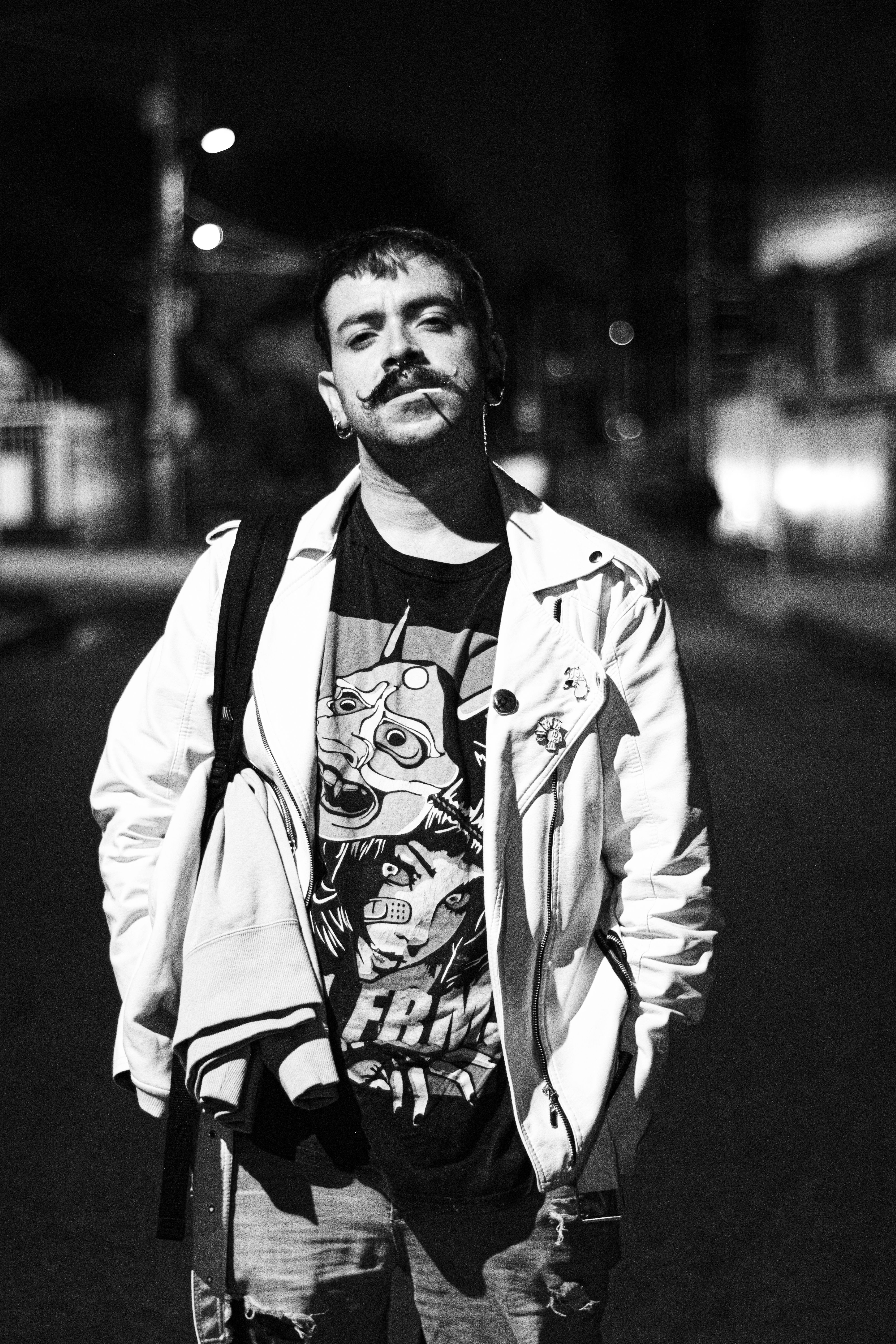 Black and white portrait of a man with a unique style posing on a Bogotá street at night.
