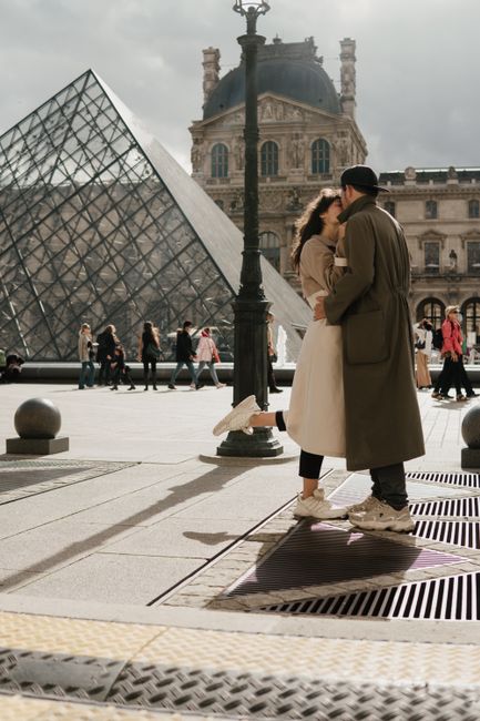 A couple shares a romantic kiss in front of the iconic Louvre Pyramid in Paris.