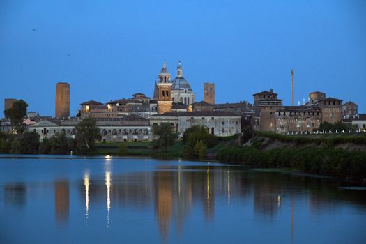 Scenic view of Mantova's historical skyline reflected on a lake during twilight, showcasing Italian architecture.