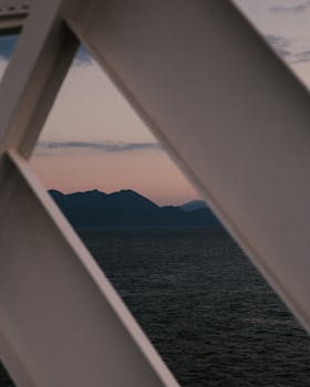 Calm ocean with mountains visible through architectural frame at sunset.