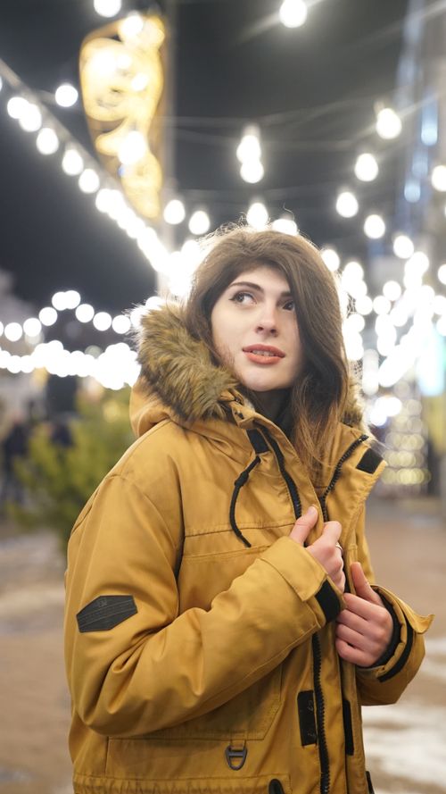 Free A woman in a yellow jacket enjoys a festive winter evening with lights. Stock Photo
