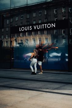 A couple strolls in front of a Louis Vuitton store at night, capturing urban lifestyle and high fashion.