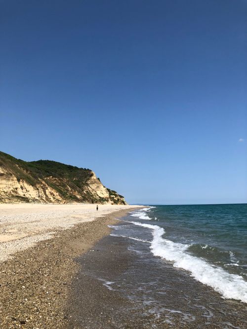 Free A tranquil beach scene featuring cliffs, calm ocean waves, and a blue sky for a serene atmosphere. Stock Photo