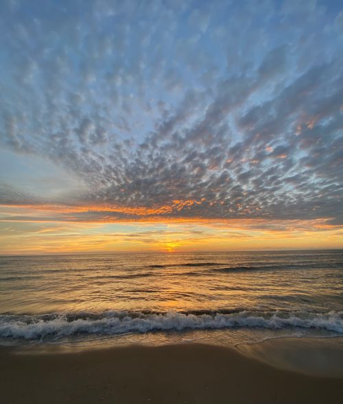 Free A peaceful beach scene at sunset with stunning clouds and gentle waves. Stock Photo