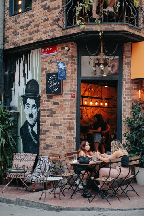 Free Two women enjoying a relaxing day at a café with a brick facade and wall art. Stock Photo