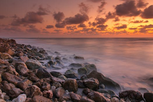 A serene view of the rocky seaside with a vibrant sunset sky, offering a calming natural landscape.