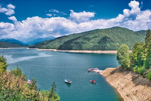 Aerial view of a tranquil lake surrounded by lush hills and boats near Cârțișoara, Romania.