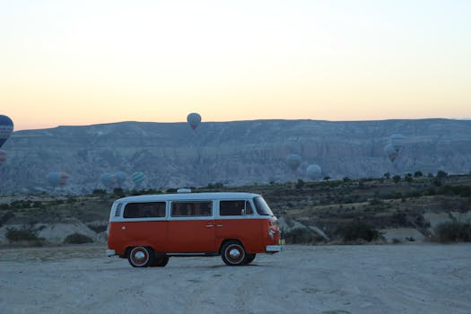 Retro Volkswagen van set against hot air balloons floating in a scenic sunrise.