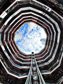 Unique upward perspective of The Vessel in NYC with sky and clouds framed by architecture.
