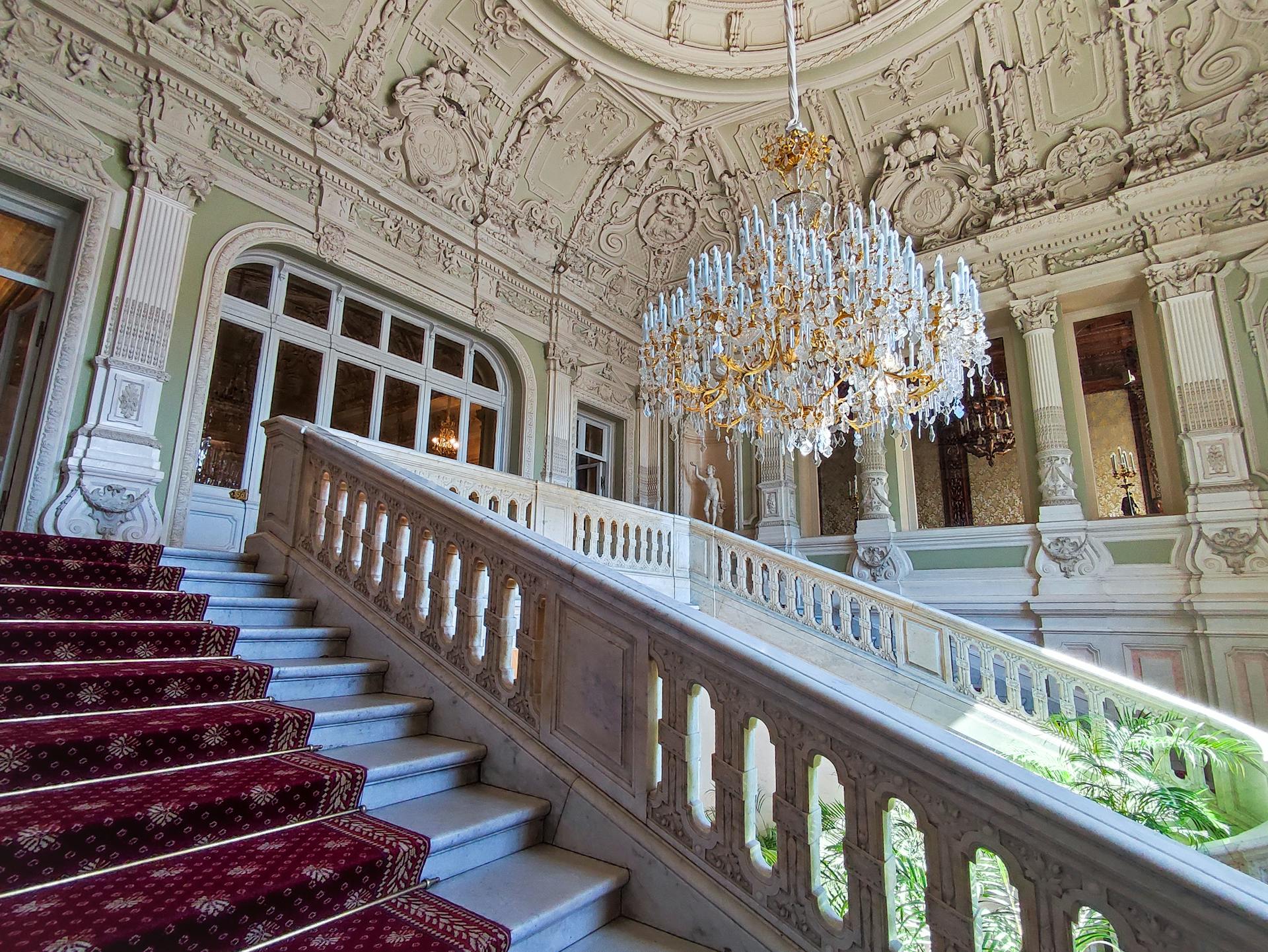 Luxurious mansion interior featuring an ornate staircase and magnificent chandelier.