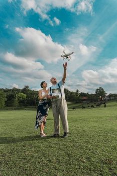 A couple enjoying their time flying a drone in a sunny park with clear skies and lush greenery.
