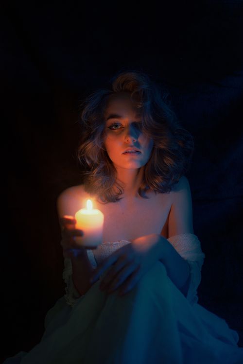 Free A woman holding a candle casts a soft, mysterious glow in this elegant portrait. Stock Photo