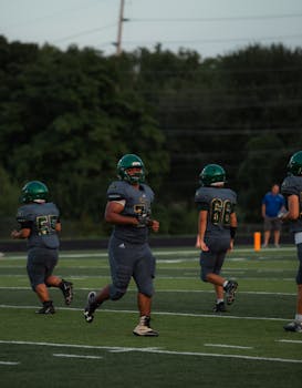 Youth football players in action on a green field, wearing helmets and uniforms.