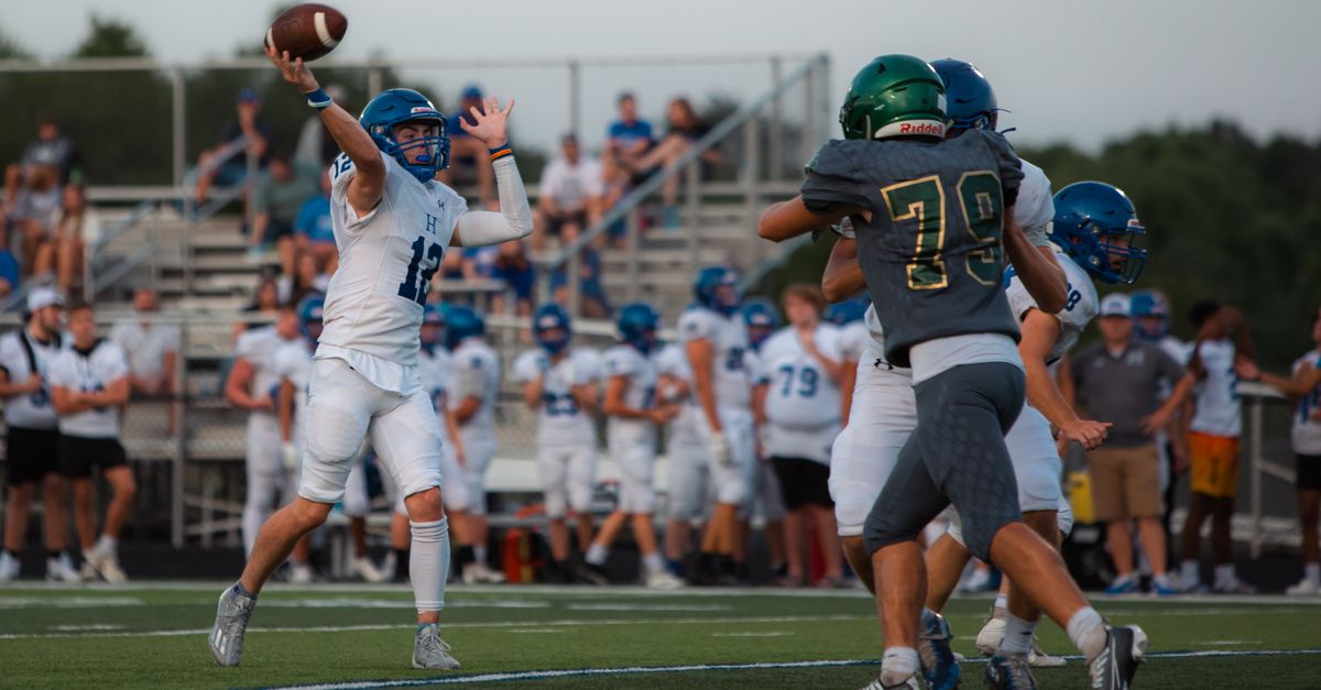 High school football game with quarterback throwing a pass under pressure.