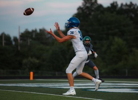 High school football players in action on the field catching a pass during a game.