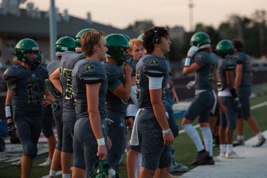 A high school football team stands on the sidelines of a field, ready for action.