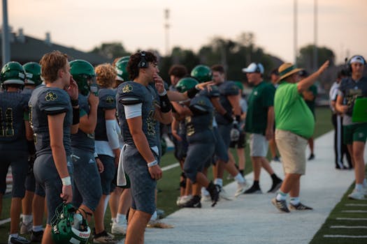 High school football team at the sideline during a game, showcasing teamwork and strategy.