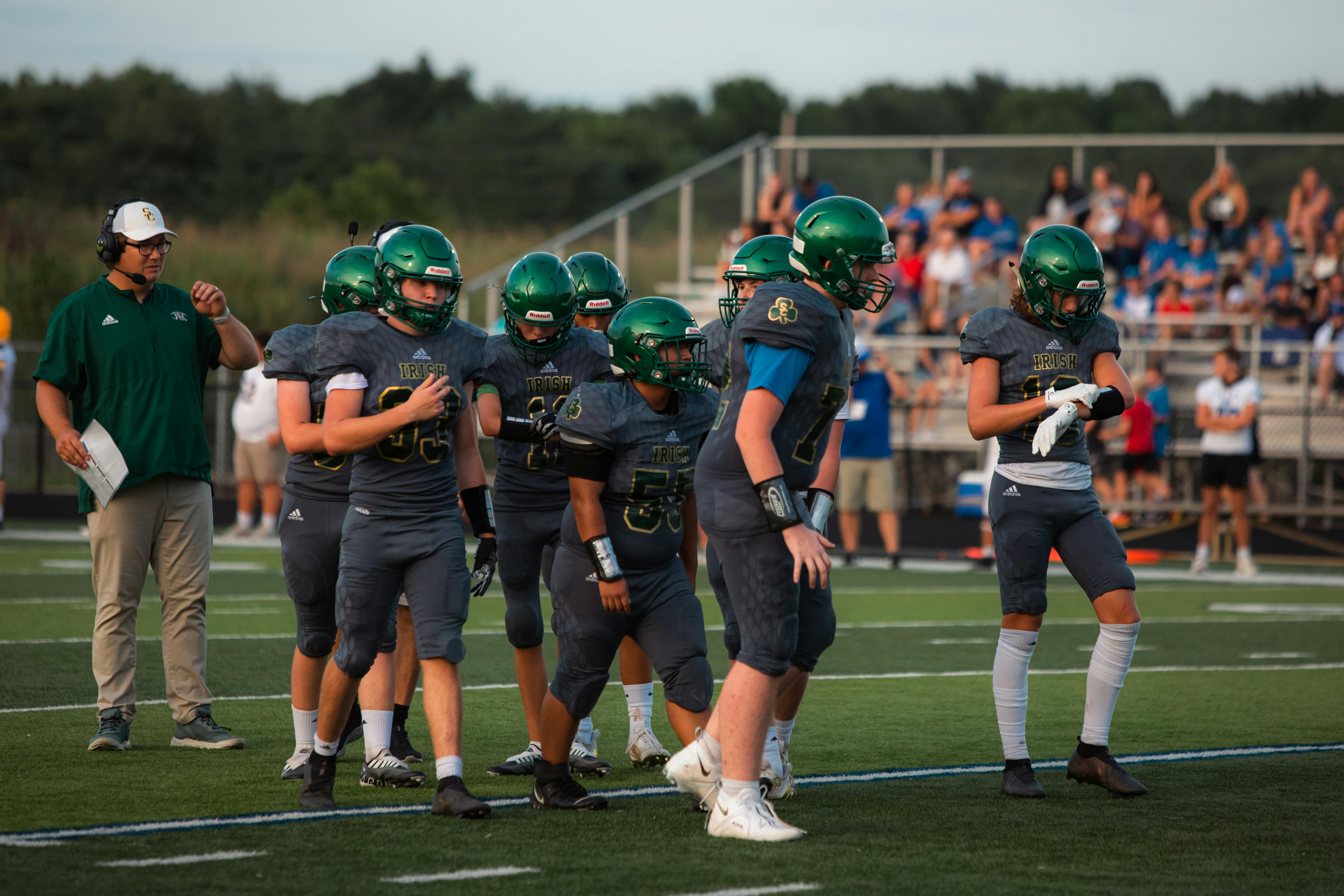 Athletes getting ready on the football field during daylight with crowd in background.