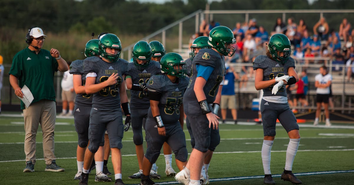 Athletes getting ready on the football field during daylight with crowd in background.