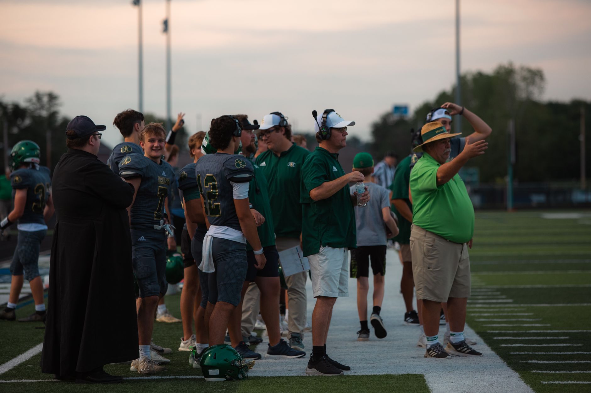 Coaches and players on high school football sidelines during a game.