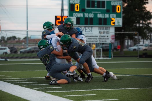 Football players engaged in an intense tackle during a high school game on a green field.