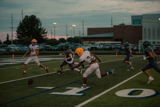 Football players in action during an evening high school game with dramatic sky backdrop.