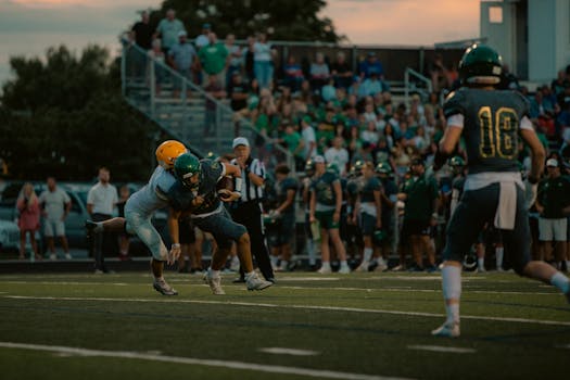 Intense tackle during a high school football game at the stadium with a crowd cheering.