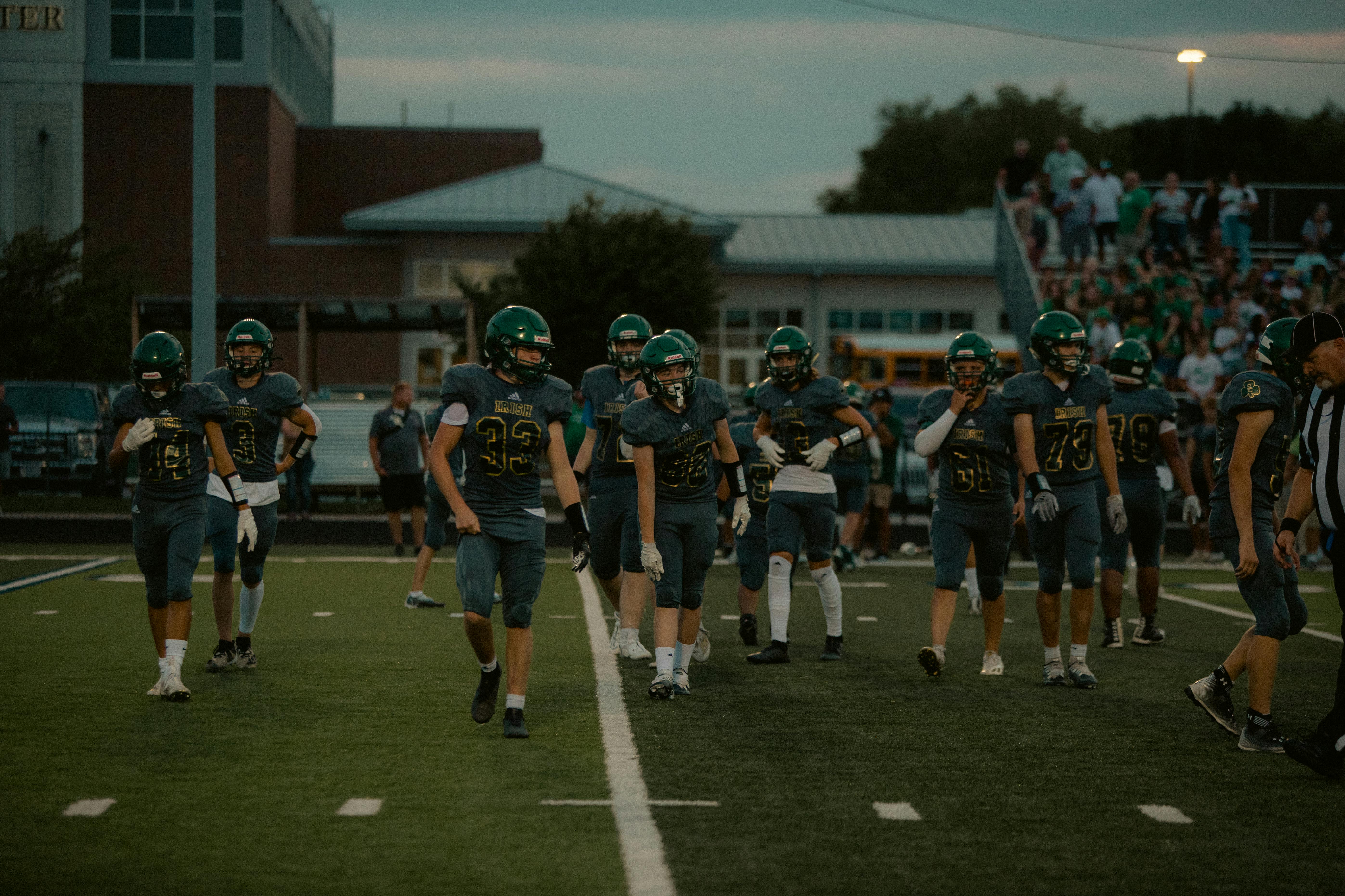 High school football players on the field preparing for a game in the evening.