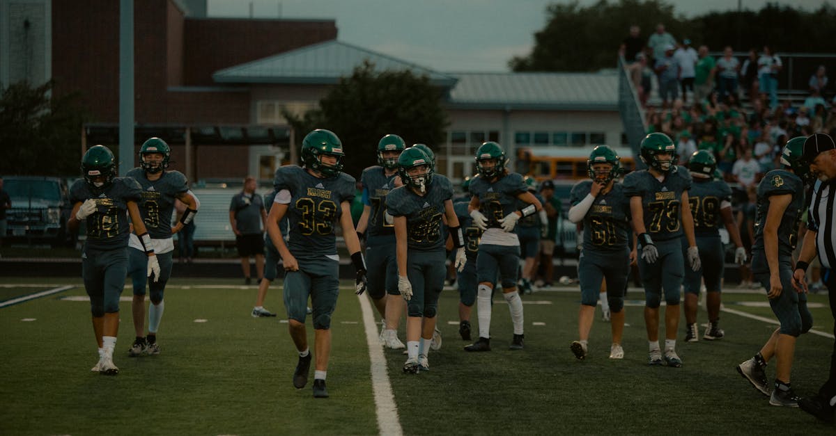 High school football players on the field preparing for a game in the evening.