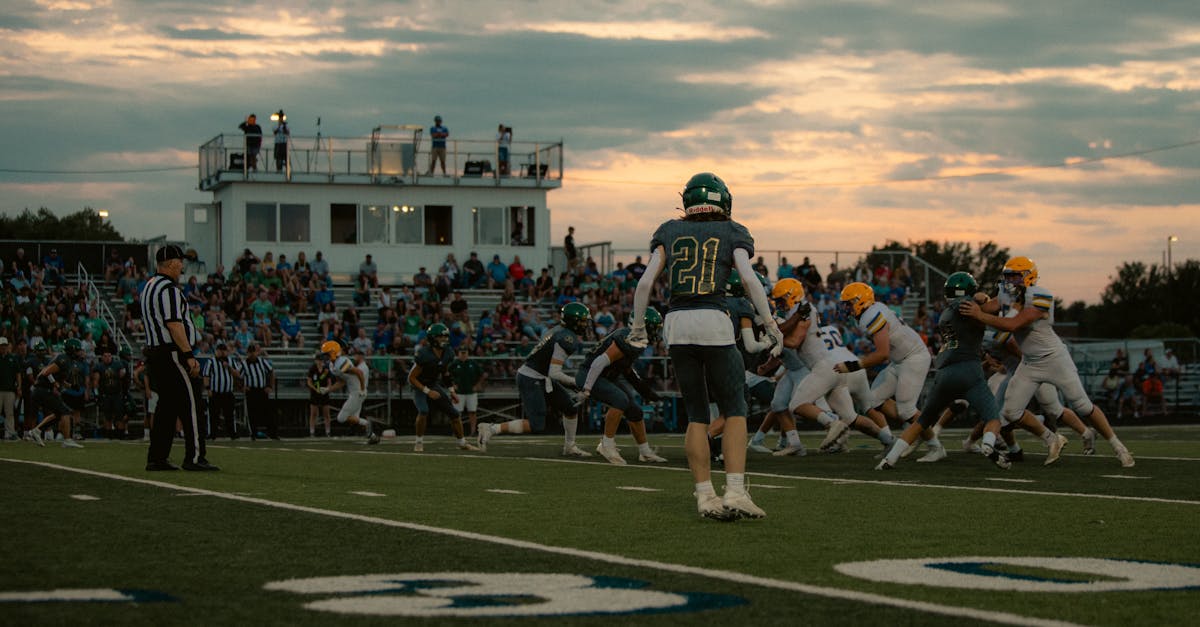 High school football game at sunset with players and crowd in action.