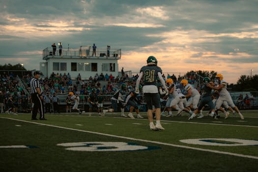 High school football game at sunset with players and crowd in action.