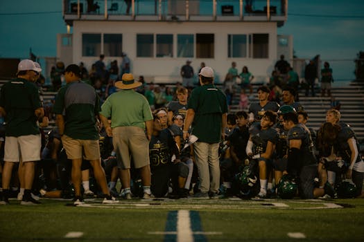 A high school football team huddles during a night game, planning their next move.