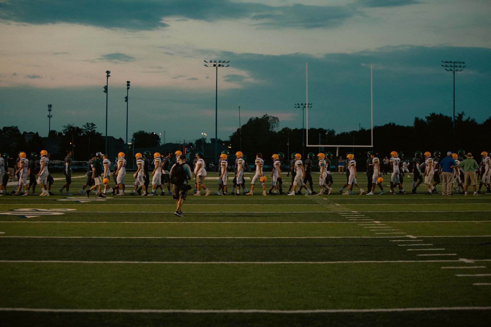 Players walking off football field at dusk after the game ends.