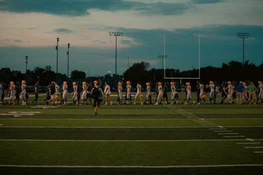 Players walking off football field at dusk after the game ends.