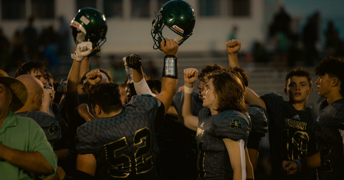 A football team celebrates victory on the field, raising helmets in teamwork and triumph.