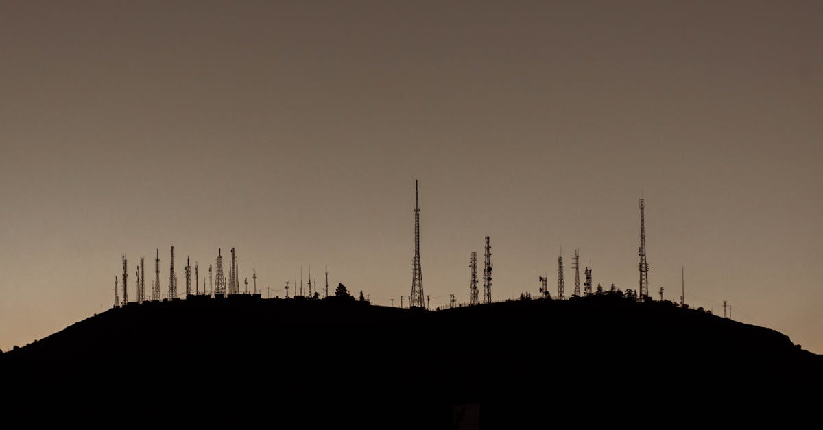 Silhouette of numerous communication towers on a hill during sunset.