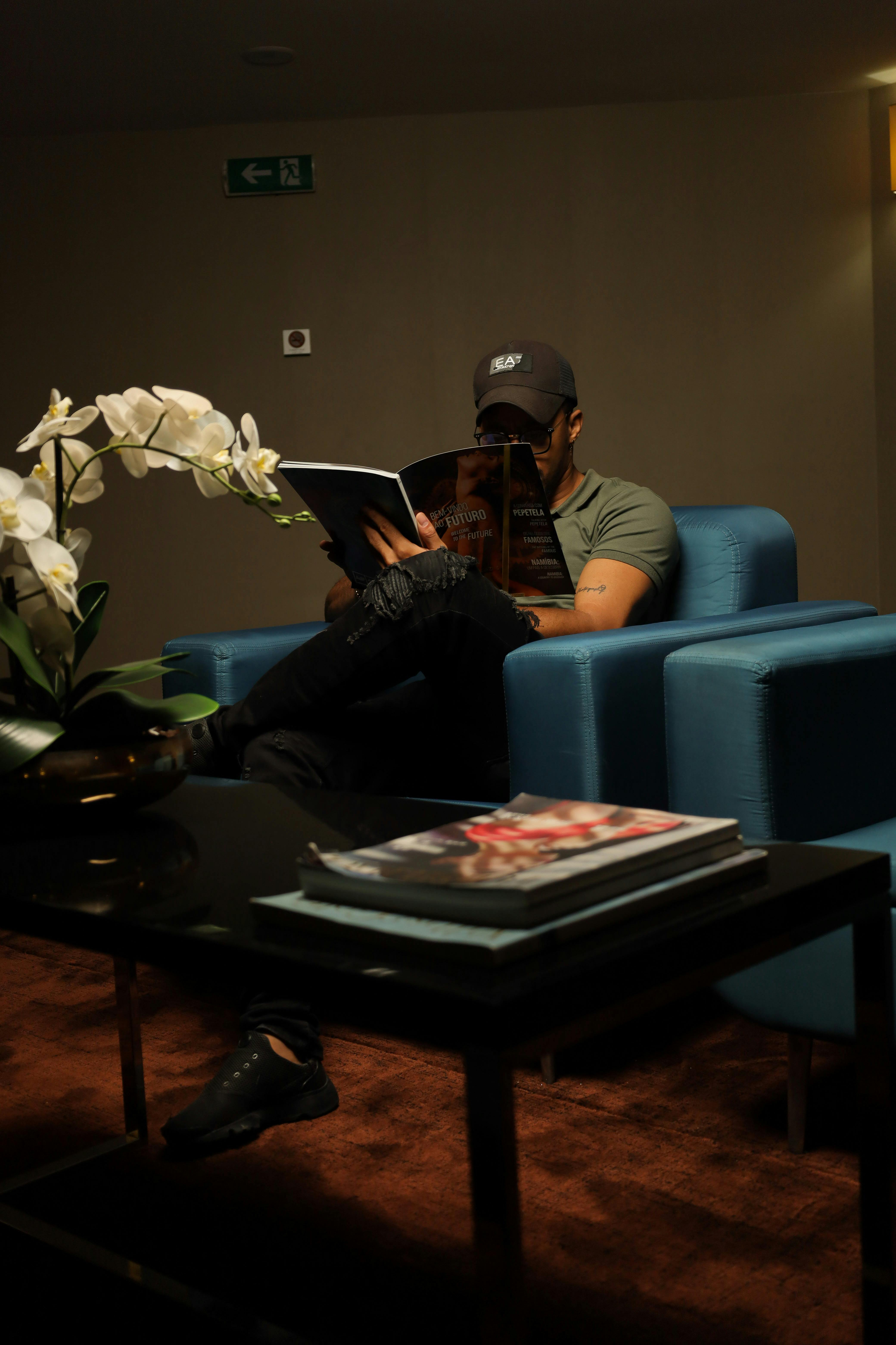 A man comfortably reading a magazine on a blue sofa in a cozy indoor setting.