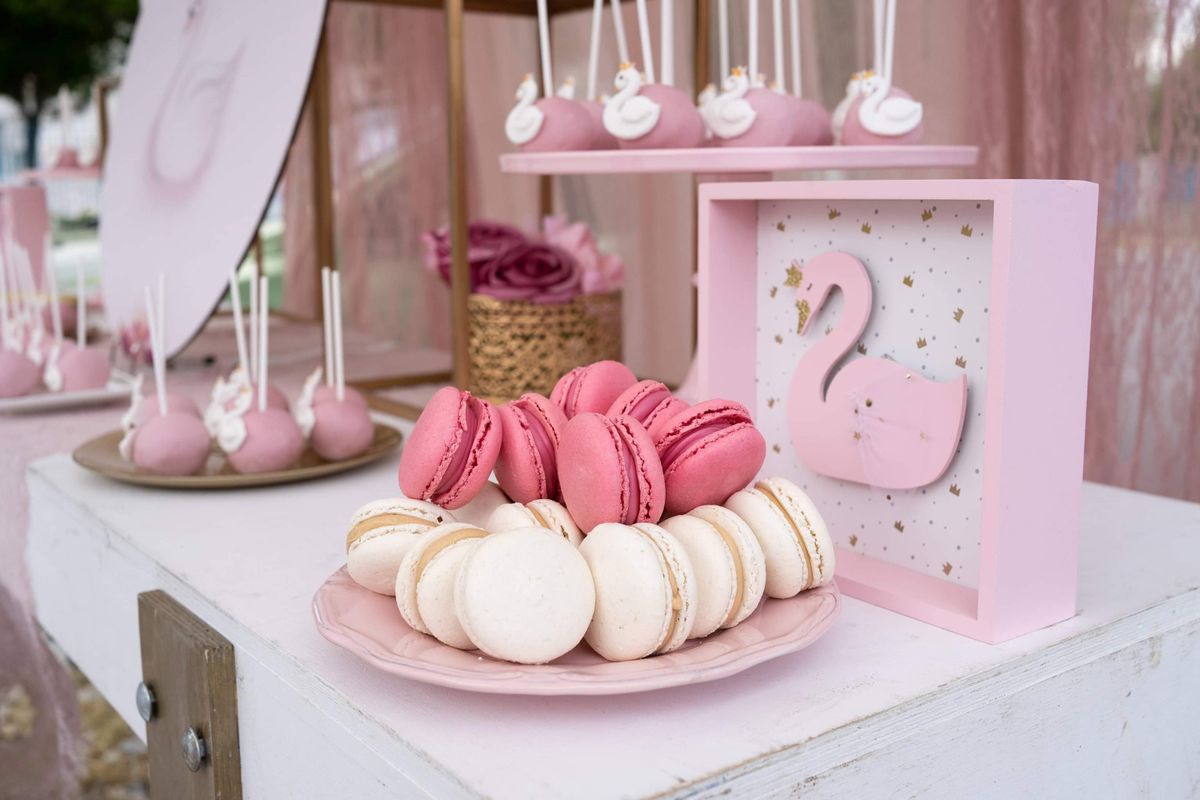 Stylish dessert table setup with pink and white macarons and swan-themed decor. Stock Photo.