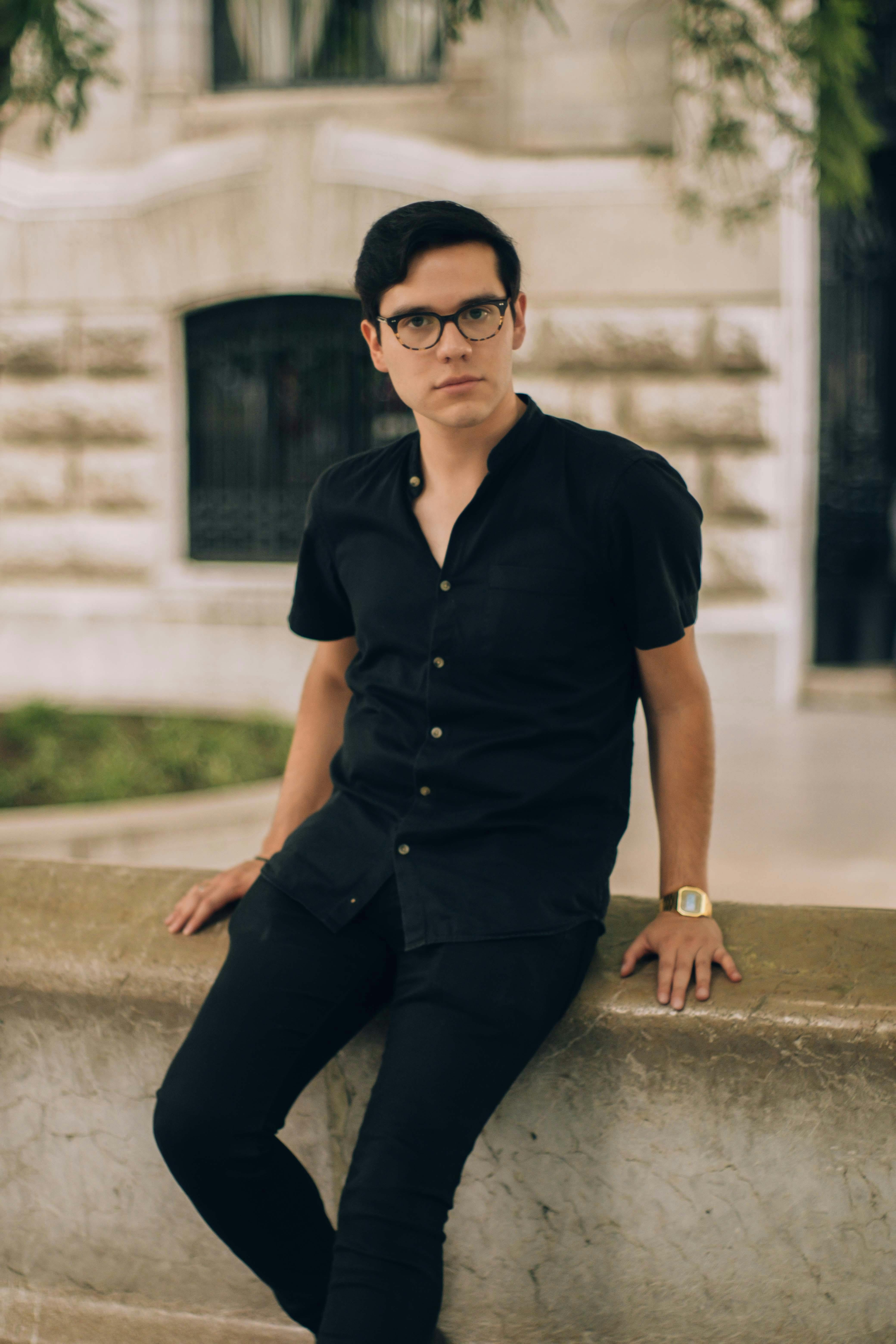Young man in black attire poses confidently outdoors in Mexico City, showcasing urban fashion.