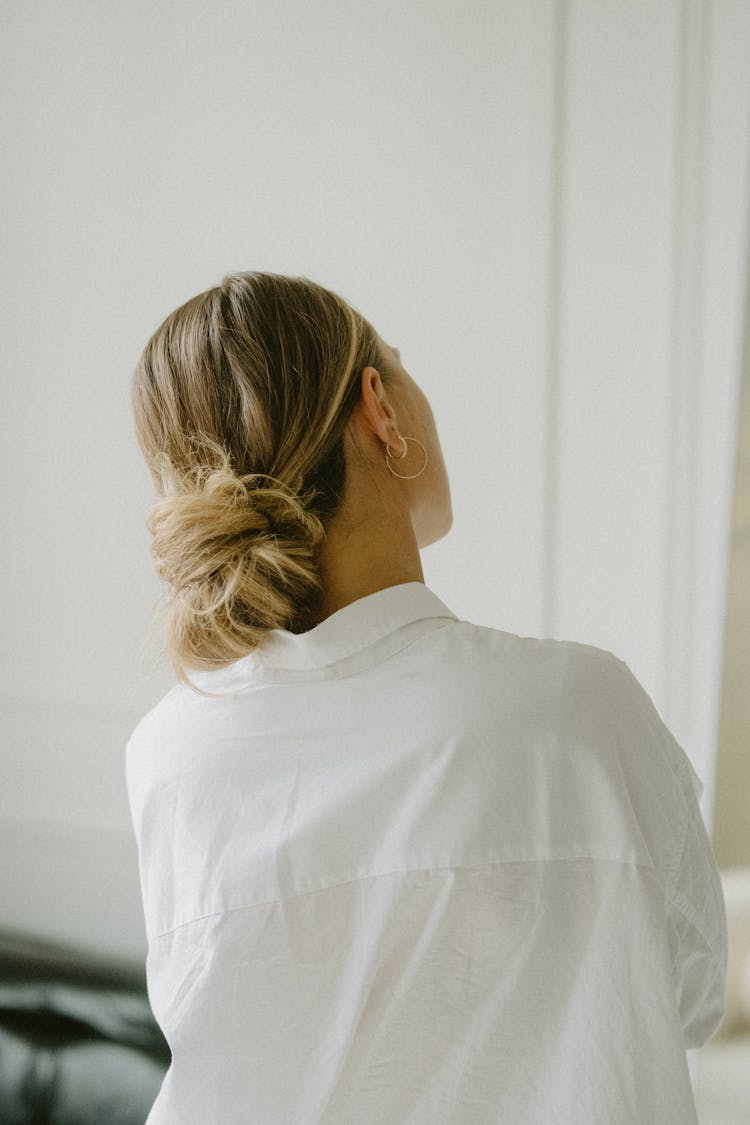 Back View Of A Woman In A White Shirt And Hair In A Low Bun 