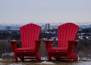 Two red Muskoka chairs facing the Toronto skyline on a winter day.