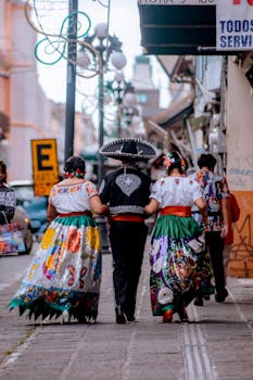 People in traditional Mexican clothing walk down a street in Puebla during a cultural celebration.