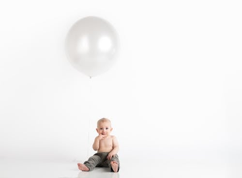 Baby Boy Sitting With White Inflatable Balloon Above